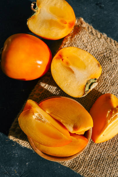 istock Sliced and whole persimmons arranged on a dark textured surface with natural light and burlap, showcasing vibrant colors and rustic simplicity. Perfect for food, seasonal, and healthy living themes 2195052084