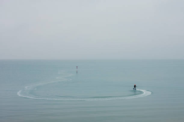 A person on an electric powered motor board making gentle waves around a waterway marker.