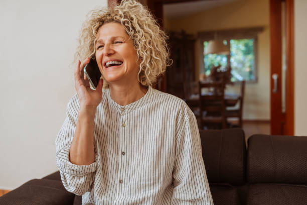 istock Happy senior woman laughing while talking on mobile phone at home 2195064451