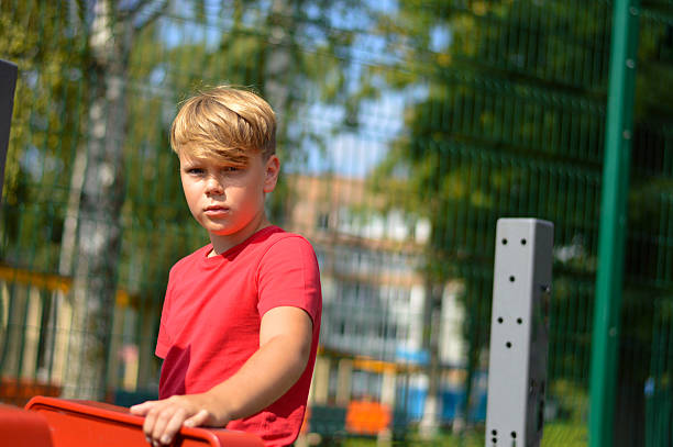 Boy exercising on outdoor exercise equipment in public playground during daytime physical activity and fitness training.