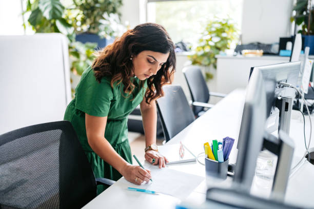 istock Mid-Adult Indian Woman Writing In A Notebook While Working On The Computer In The Office Building In Sydney In Australia 2195087667
