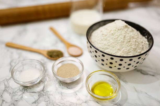 Various ingredients for crafting food including flour, milk, spices, and oil are displayed on a white marble surface, showcasing an arrangement suitable for homemade cooking and baking preparations