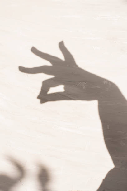 shadow of a hand with two fingers clasped on a light textured surface. elegance, dance. copy space