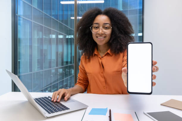 istock Smiling professional showcasing smartphone screen while working on laptop at desk 2195091565