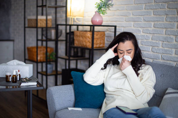 istock Sick woman sits on the couch and wipes her nose with a handkerchief 2195092995