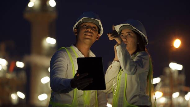 istock Two engineers in safety gear using a tablet and phone to discuss operations at a brightly lit power plant during nighttime. 2195093057