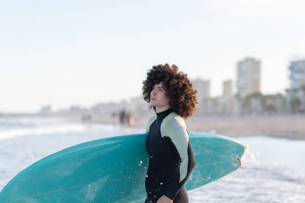 istock Curly haired woman with surfboard on sea shore 2195095855