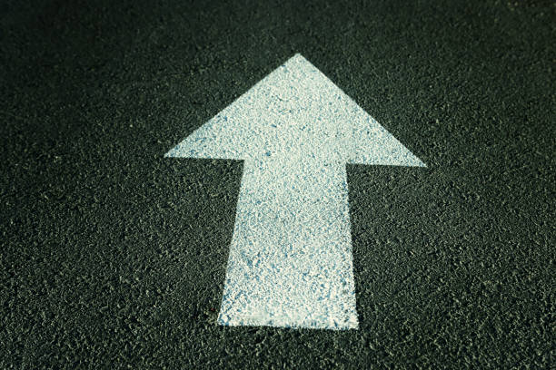 White arrow sign on asphalt pointing ahead