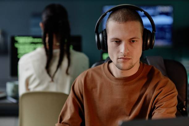 istock Portrait of Male IT Developer in Headphones Coding on Laptop while Working in Office with Colleagues 2195099689