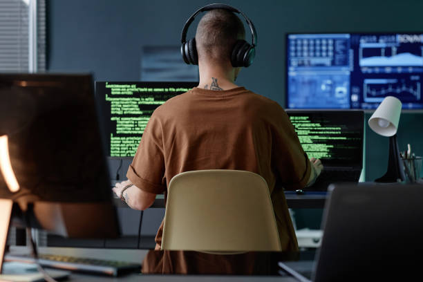 istock Back of Male Programmers in Headphones Working at Desk with Computers in Office 2195099701