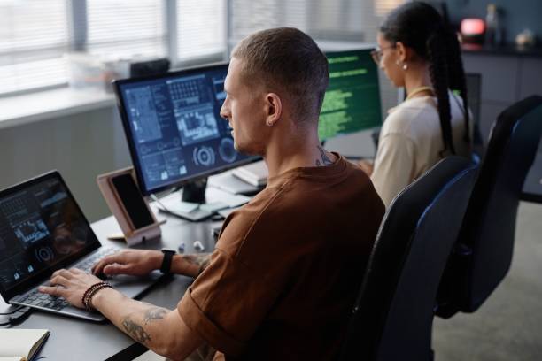 istock Side View of Male IT Programmer with Earring Coding on Laptop at Working Desk in Office 2195099750