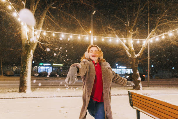 A smiling woman with a red scarf enjoys a snowy winter day in a serene forest setting beneath a bright blue sky. Christmas and New Year celebration concept.