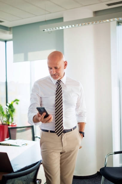istock Mid aged businessman using his smartphone and standing in a high-end office 2195109891