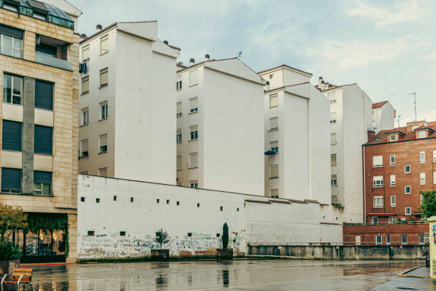 White residential buildings with a graffiti-covered wall in the foreground, surrounded by urban structures under a cloudy sky. Captures urban life and contrast.