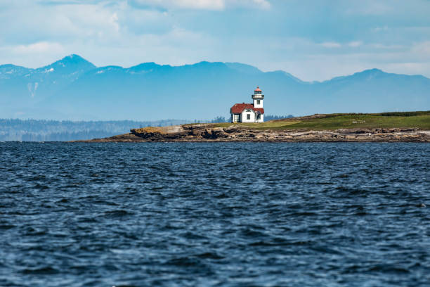 A picturesque lighthouse situated by the coastline with mountains in the background and calming ocean waters, evoking a sense of serenity and coastal charm.