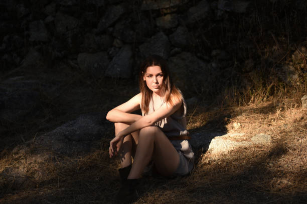 Model is sitting on the ground near old stone wall