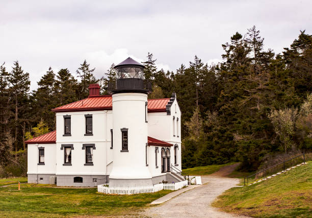 Elevated view of the historic Admiralty Head Lighthouse, nestled on Whidbey Island with a backdrop of lush evergreen forest, showcasing a blend of rustic charm and maritime heritage under an overcast sky.