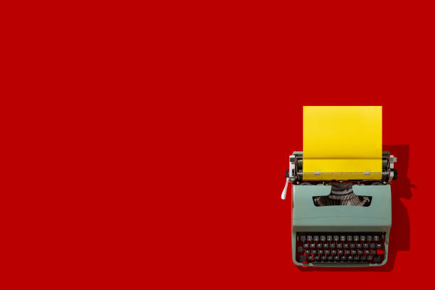 A vintage typewriter sits ready for use, featuring a bold yellow sheet of paper. The striking red backdrop enhances the classic aesthetics of this writing tool, inviting creativity and inspiration.