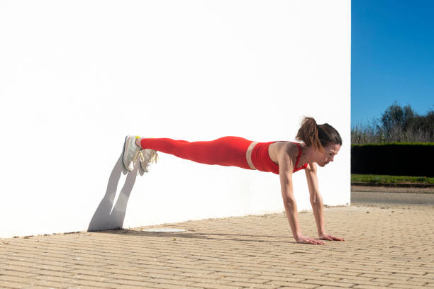 istock Athletic woman female performing plank exercise outdoors against white wall, 2195126228