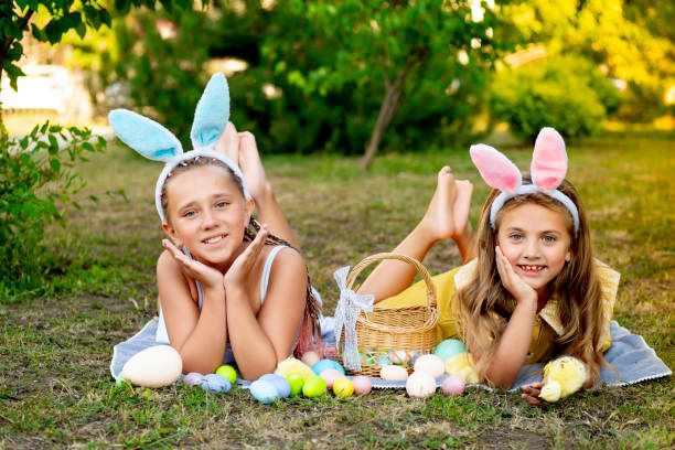 istock Easter, children play with Easter eggs in bunny ears on the green lawn. Easter tradition. Children with a basket full of colorful eggs 2195126573