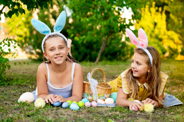 istock Easter, children play with Easter eggs in bunny ears on the green lawn. Easter tradition. Children with a basket full of colorful eggs 2195126588