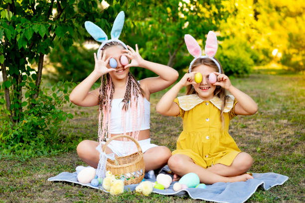 istock Easter, children play with Easter eggs in bunny ears on the green lawn. Easter tradition. Children with a basket full of colorful eggs 2195126589