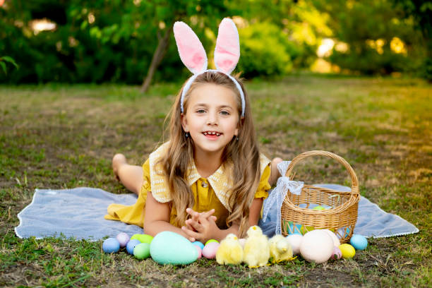 istock Easter, a baby girl is playing with Easter eggs in bunny ears on a green lawn. Easter tradition. A joyful child with a basket of colorful eggs 2195126597