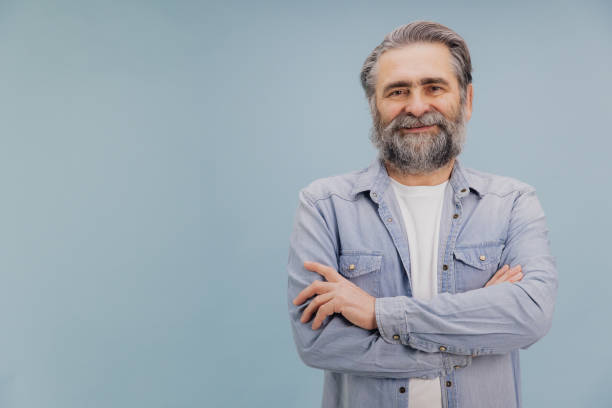 istock Smiling senior man with crossed arms and beard posing on blue background 2195133069