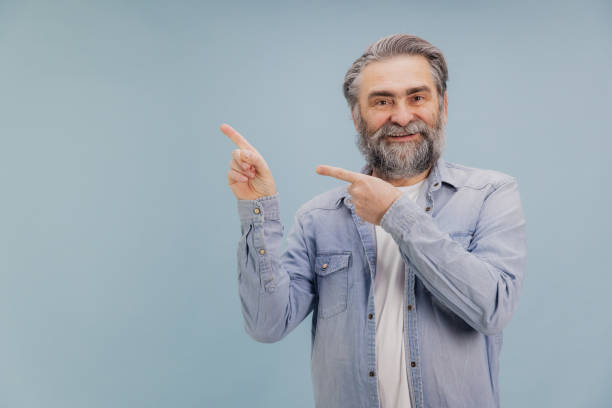 istock Smiling senior man pointing aside with both index fingers on blue background 2195133137