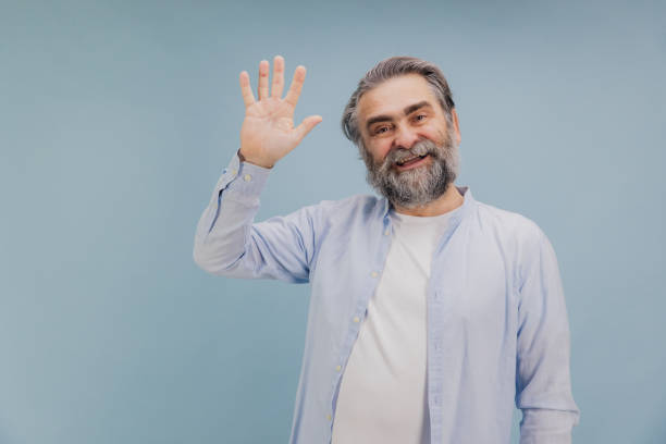 istock Smiling Senior Man Waving Hand on Blue Background 2195133344
