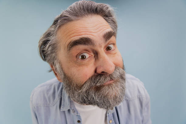 istock Curious senior man with grey beard and hair making a funny face on blue background 2195133513