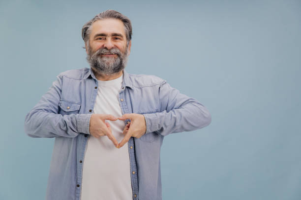 istock Smiling senior man making heart shape with hands on blue background 2195134742
