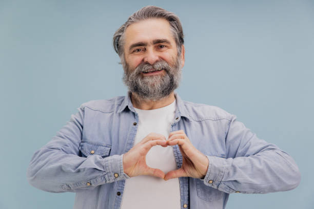 istock Senior man making heart shape with hands on blue background 2195134747
