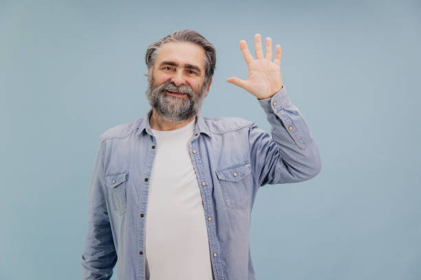 istock Smiling senior man waving hand on blue background 2195134754