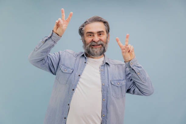 istock Happy Senior Man Showing Victory Sign with Both Hands on Blue Background 2195134762