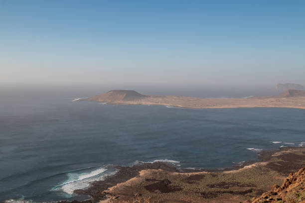View from a cliff on the coast and Atlantic ocean. Land of island La Graciosa in the background. Blue evening sky with a touch of pink. Mirador de Guinate, Lanzarote, Canary Islands, Spain.