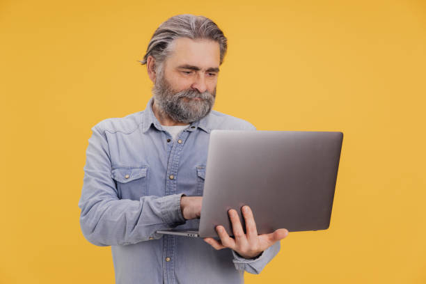 istock Senior man using laptop on yellow background 2195135369