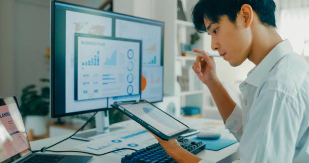 istock Closeup of young Asian man working from home, using digital tablet for financial data analysis modern remote work environment. Remote work and finance. 2195136960