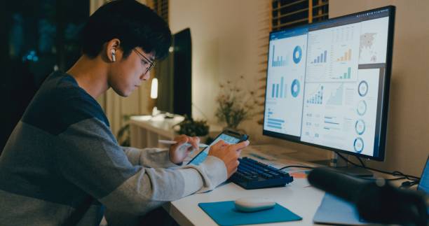 istock Young Asian man financial advisor working late at home, using a tablet and laptop, discussing strategy with clients via video call, showcasing remote work efficiency. Remotely and finance. 2195137133