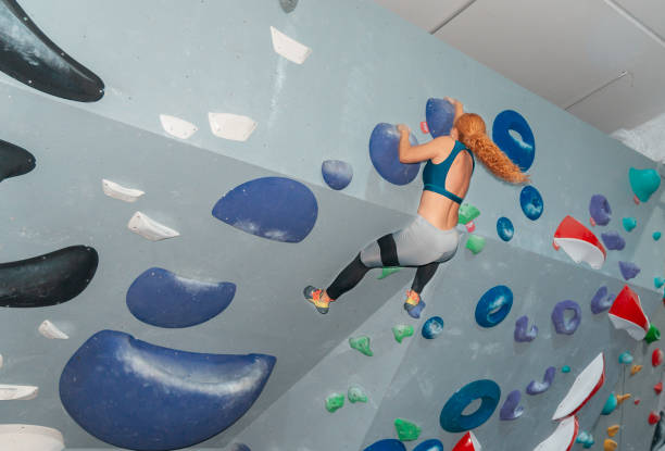 Sporty little girl climbing artificial boulder on practical wall in gym