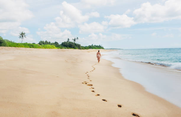 istock Young female dressed in light summer clothes walking barefoot leaving footprints on the sand on Indian ocean Tangalle lonely coconut trees beach on Sri Lanka island. Aerial top view drone shot. 2195143942