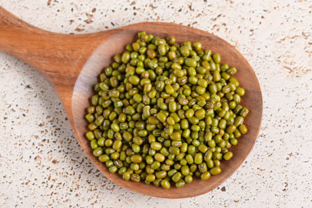istock Mung beans in a wooden spoon on beige kitchen table background, top view 2195150898