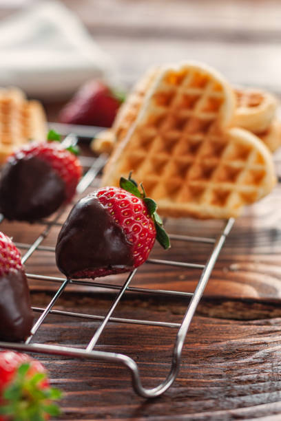 three chocolate covered strawberries in a rustic wooden bowl on a wooden table