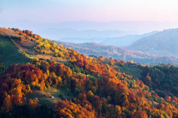 istock Fall scenery. Landscape with orange, red, green forest.     Sun rays enlighten the meadow with trees. Landscape with high mountains. 2195153956