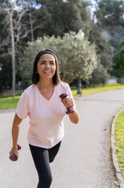 istock Mature hispanic woman jogging in a park while lifting weights, enjoying her workout routine 2195161507