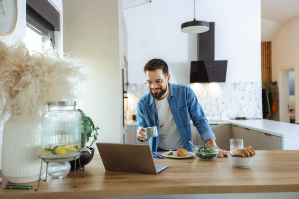 istock Man enjoying coffee and working on laptop in modern home kitchen 2195167324
