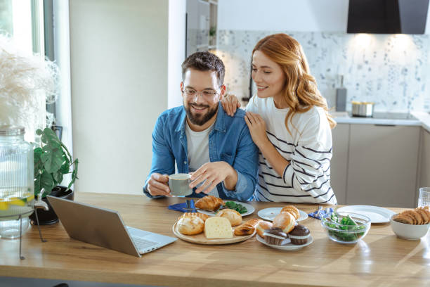 istock Couple enjoying breakfast together while using a laptop in their kitchen 2195167828