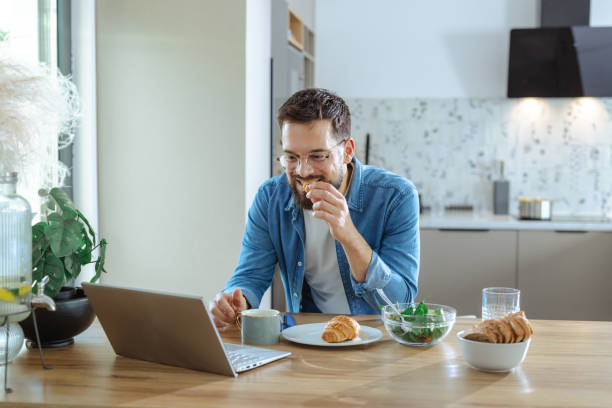 istock Man enjoying breakfast and coffee while working on laptop in kitchen 2195168049