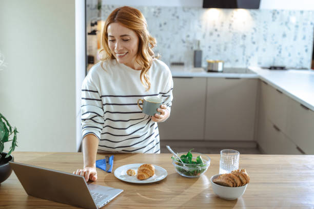 istock Woman browsing laptop while enjoying breakfast at a modern kitchen counter 2195168225