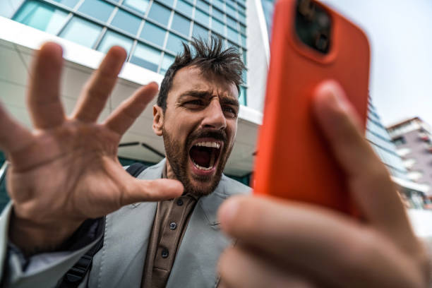 Close-up of angry male entrepreneur looking at smart phone and shouting.